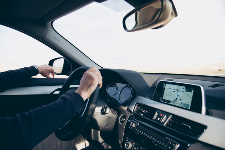 Man driving his vehicle with his hand out the window and one hand on the steering wheel.